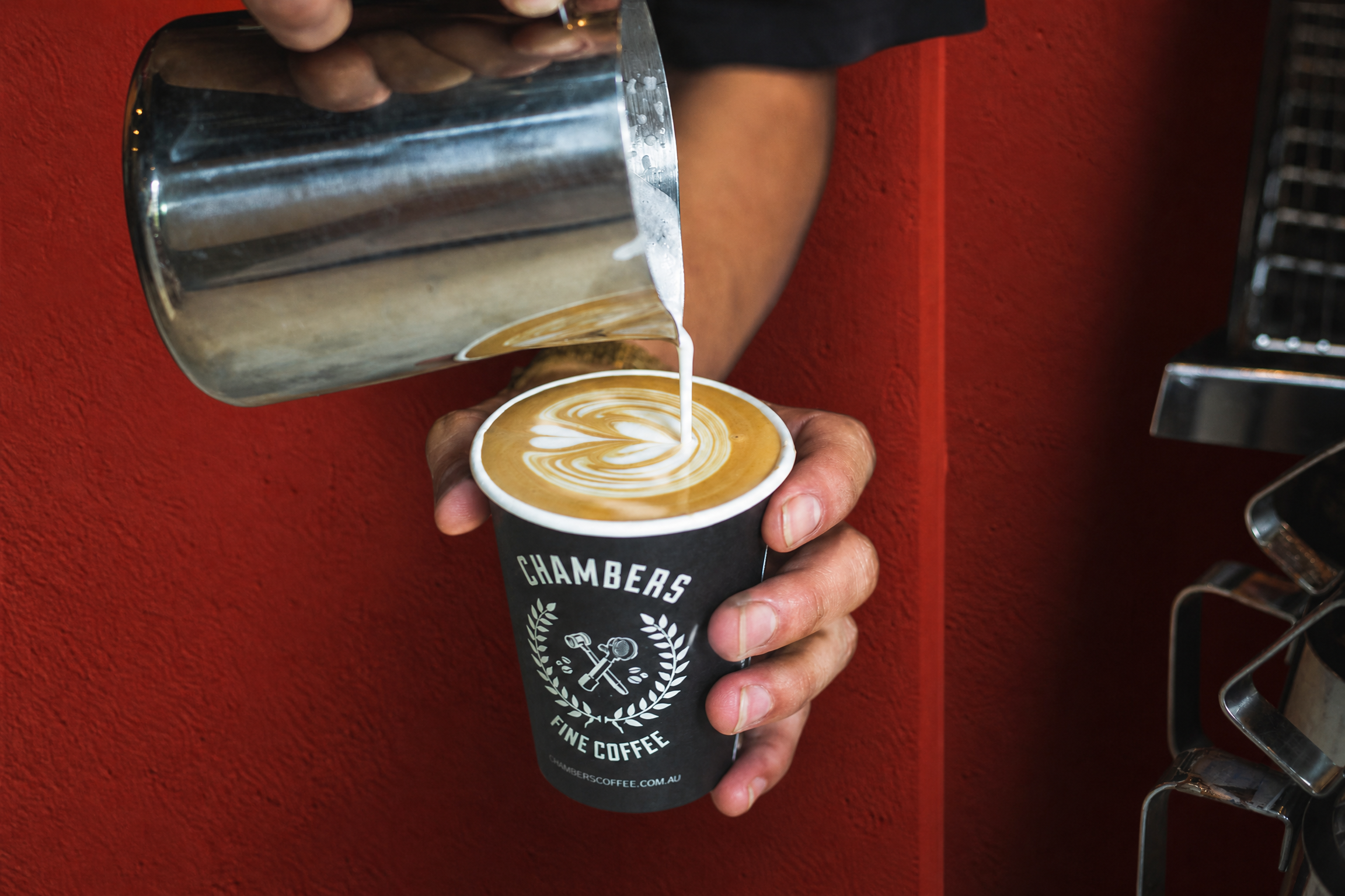 Milk being poured into a branded Chambers coffee cup against a red Sydney café service wall